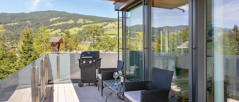 A balcony with a wooden deck, a glass door, wicker furniture, and a barbecue grill.