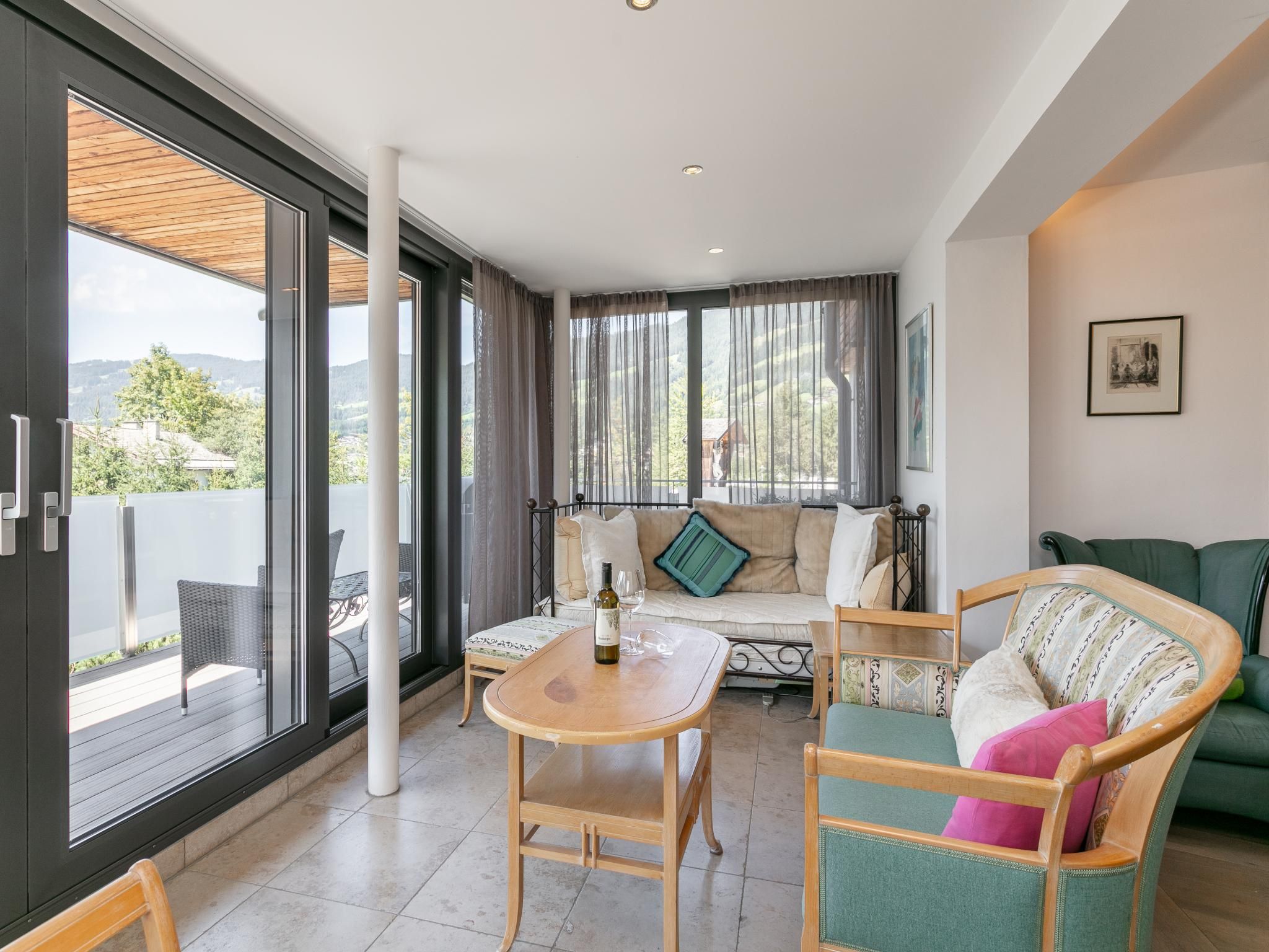 Un vaste espace de vie comprenant une table en bois, un canapé et un fauteuil. De grandes fenêtres offrent une vue sur l’extérieur.