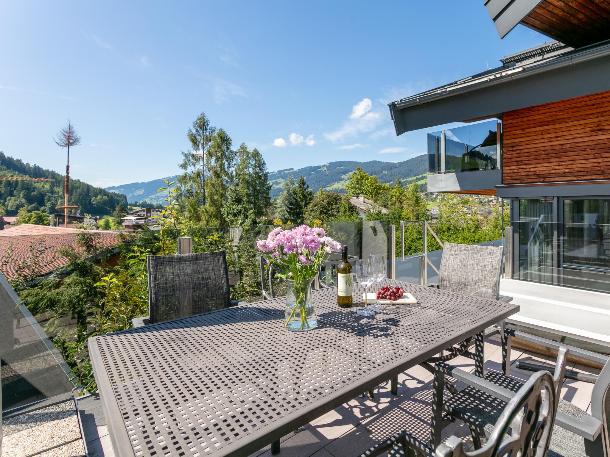Un espace de restauration en plein air avec une table, des chaises, un vase de fleurs et une bouteille de vin.