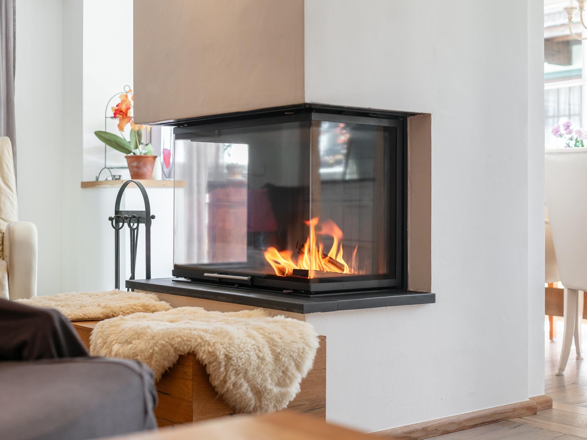 A modern fireplace with a glass front, a wooden bench in front, and a potted plant to the left.