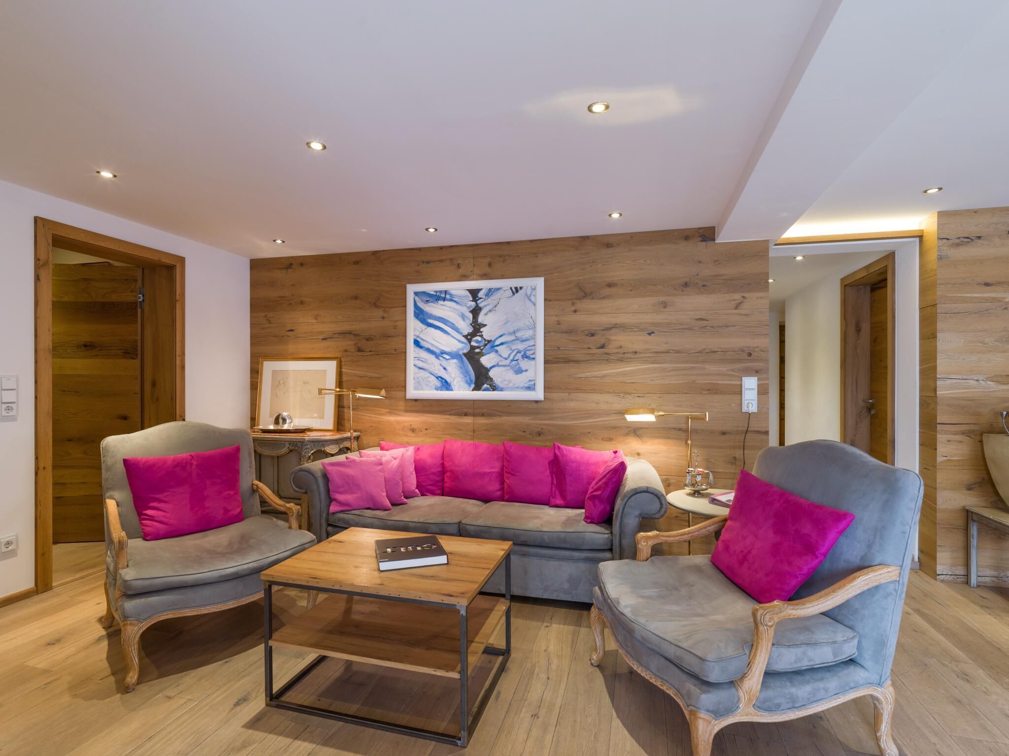 A modern living room with a wooden wall, a sofa, two armchairs, a coffee table, and a painting.
