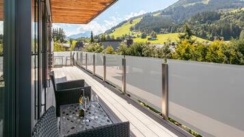 Une terrasse meublée de mobilier en osier, une bouteille de vin et des verres, le tout offrant une vue sur un paysage montagneux.