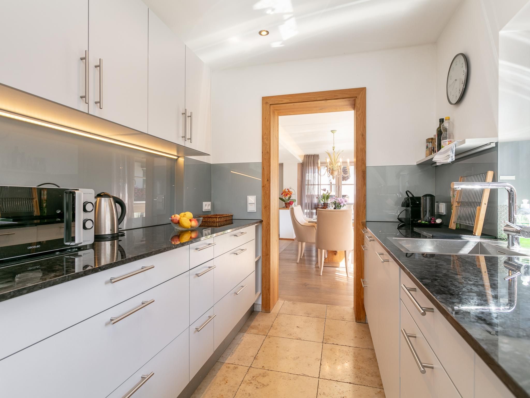 A modern kitchen with white cabinets, a black countertop, and a wooden door leading to a dining area.