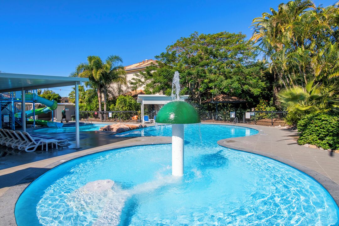 Une piscine avec une fontaine, des chaises longues et un espace abrité équipé d’un toboggan.