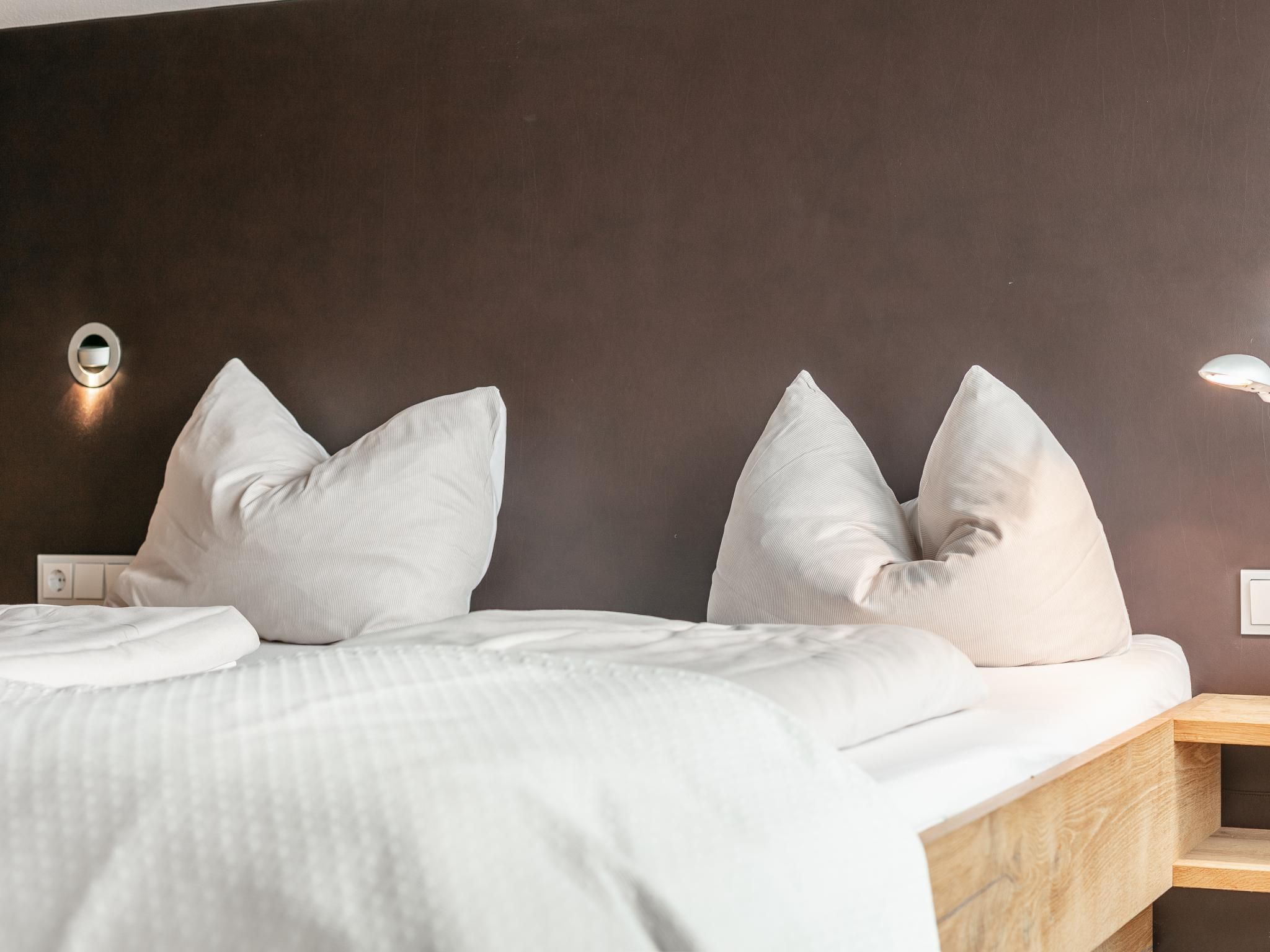 Une chambre d’hôtel comprenant un lit, des oreillers, une table de chevet et un luminaire fixé au mur.