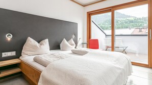 Un dormitorio moderno con una cama grande, una mesita de noche, una silla roja y vistas a un paisaje verde a través de un ventanal corredero.