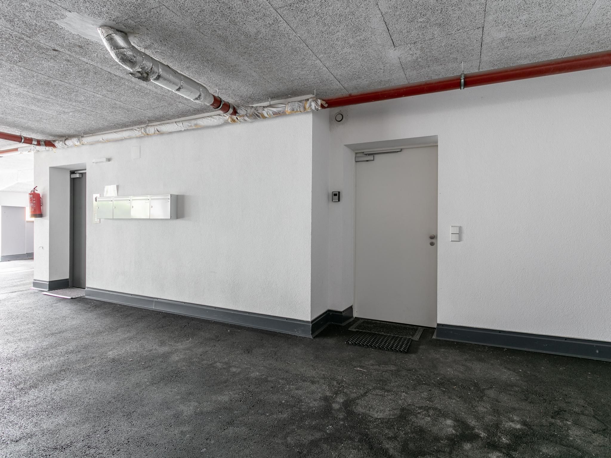 Een parkeergarage met betonnen vloeren, witte wanden en een rode pijp aan het plafond.