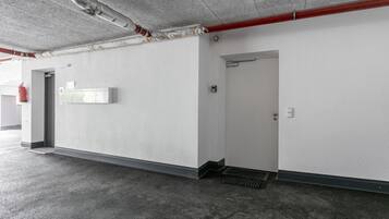 Een parkeergarage met betonnen vloeren, witte wanden en een rode pijp aan het plafond.