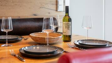 Une table à manger dressée avec des assiettes, des verres et une bouteille de vin, avec un panier en osier et une chaise rouge au premier plan.