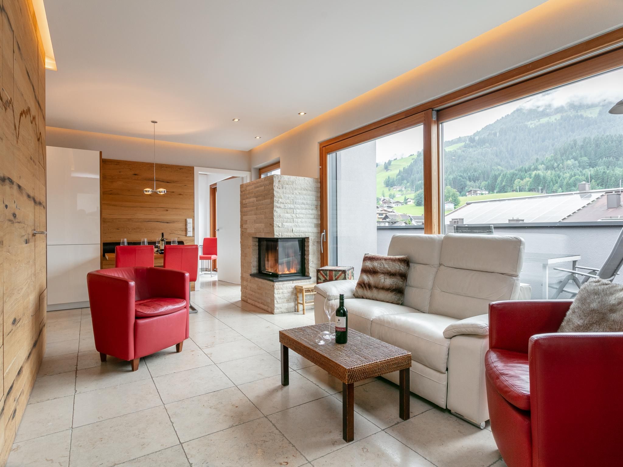 Una sala de estar moderna con chimenea, sillas rojas, un sofá y vistas al exterior.