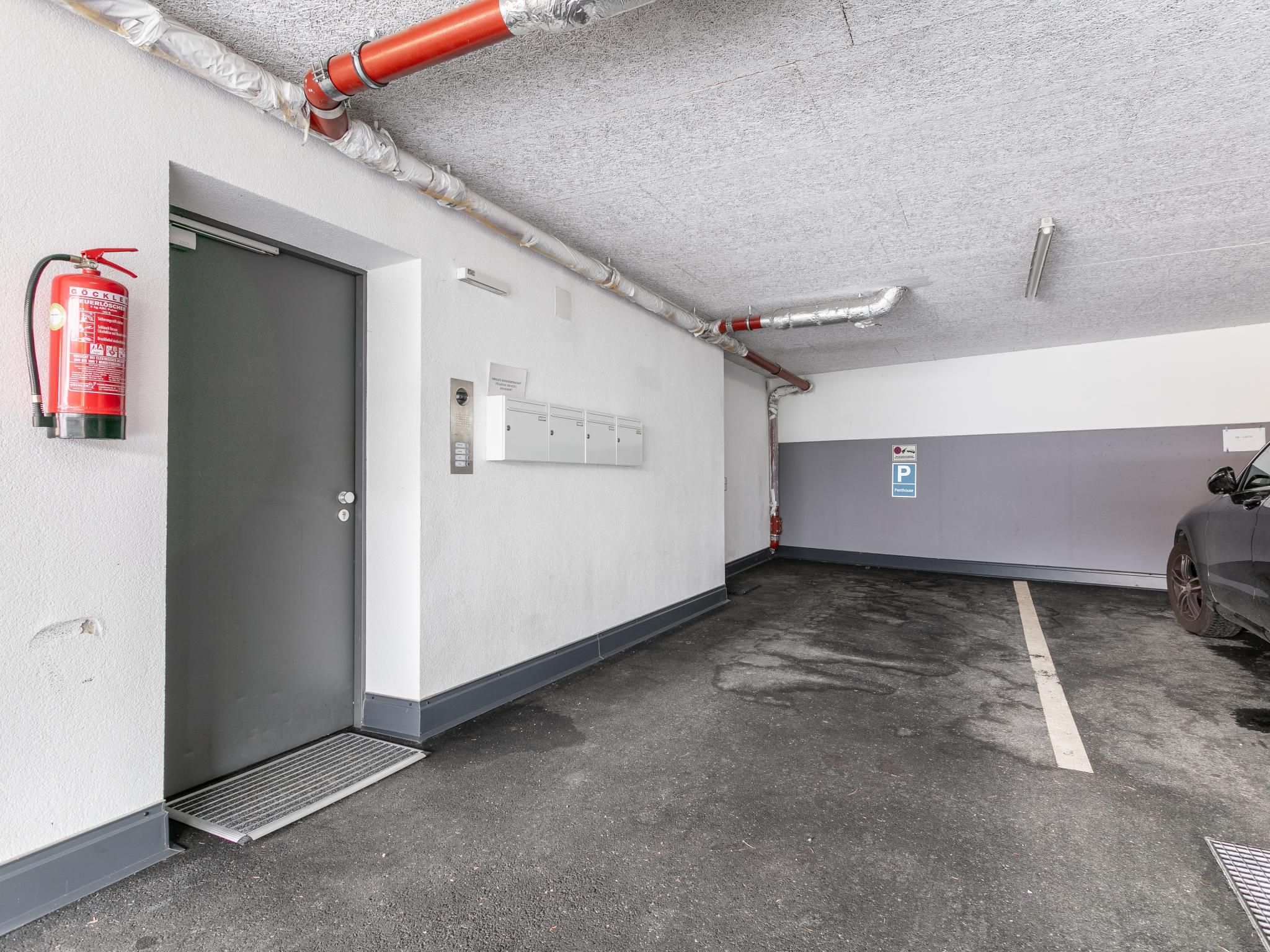 Een parkeergarage met een brandblusser aan de muur, een deur en een ventilatiesysteem.