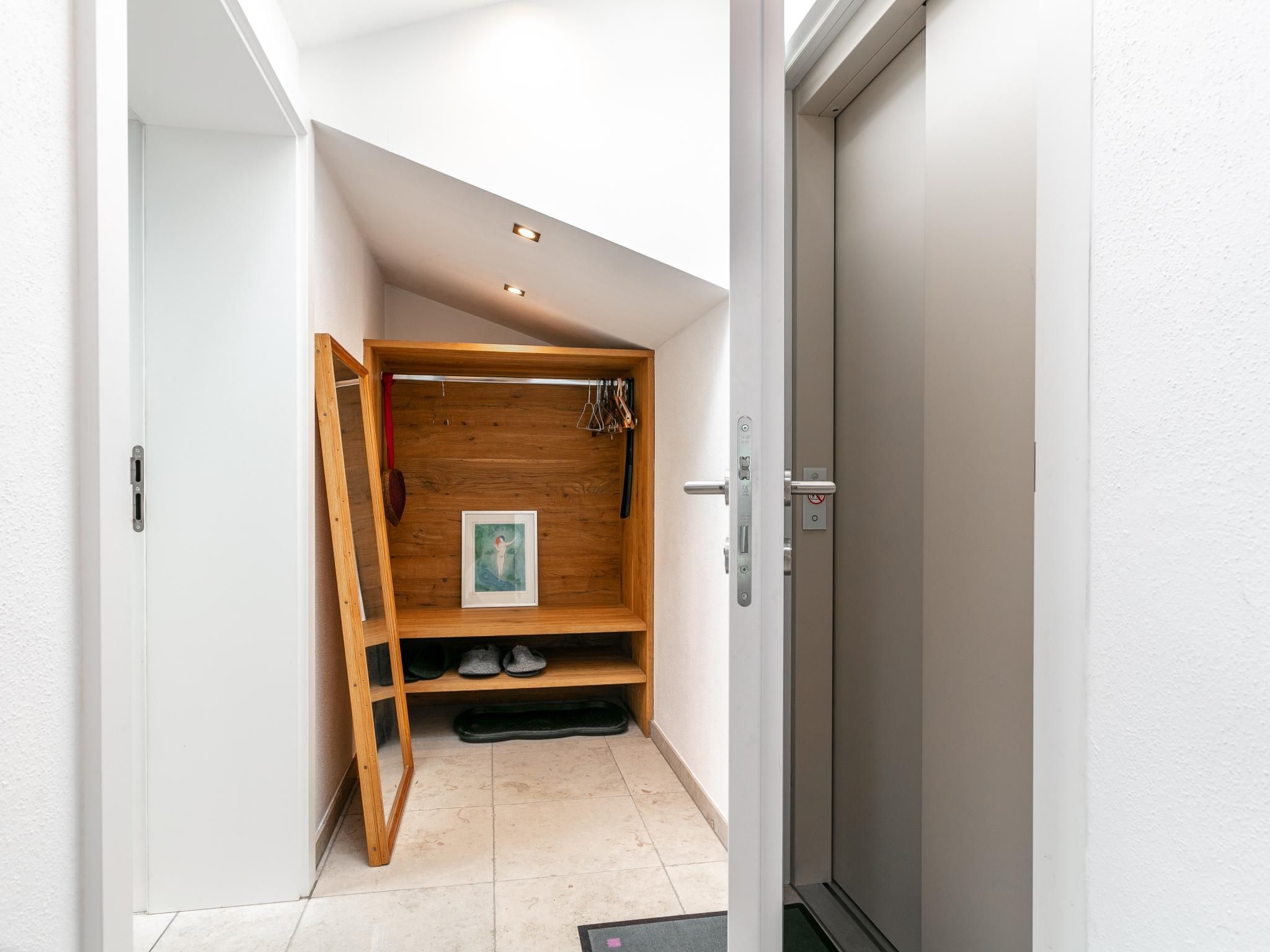 Un pasillo con un mueble de almacenamiento de madera, una puerta y suelo de baldosas.