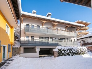 A two-story building with a balcony, a covered parking area, and snow on the ground.