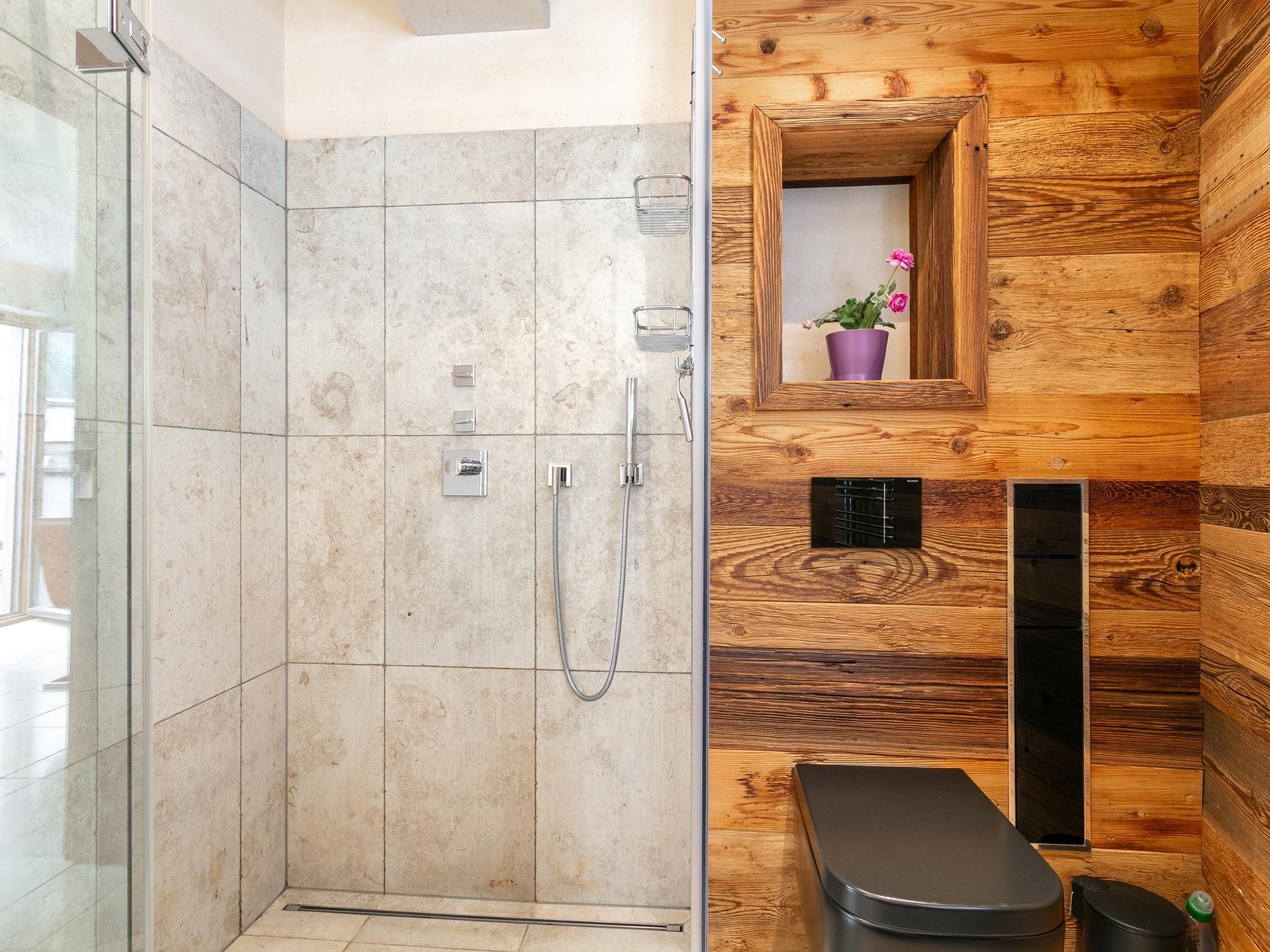 Une salle de bain moderne avec une douche  à parois de verre, un lambris mural en bois, un petit lavabo avec un receveur violet et une poubelle noire.