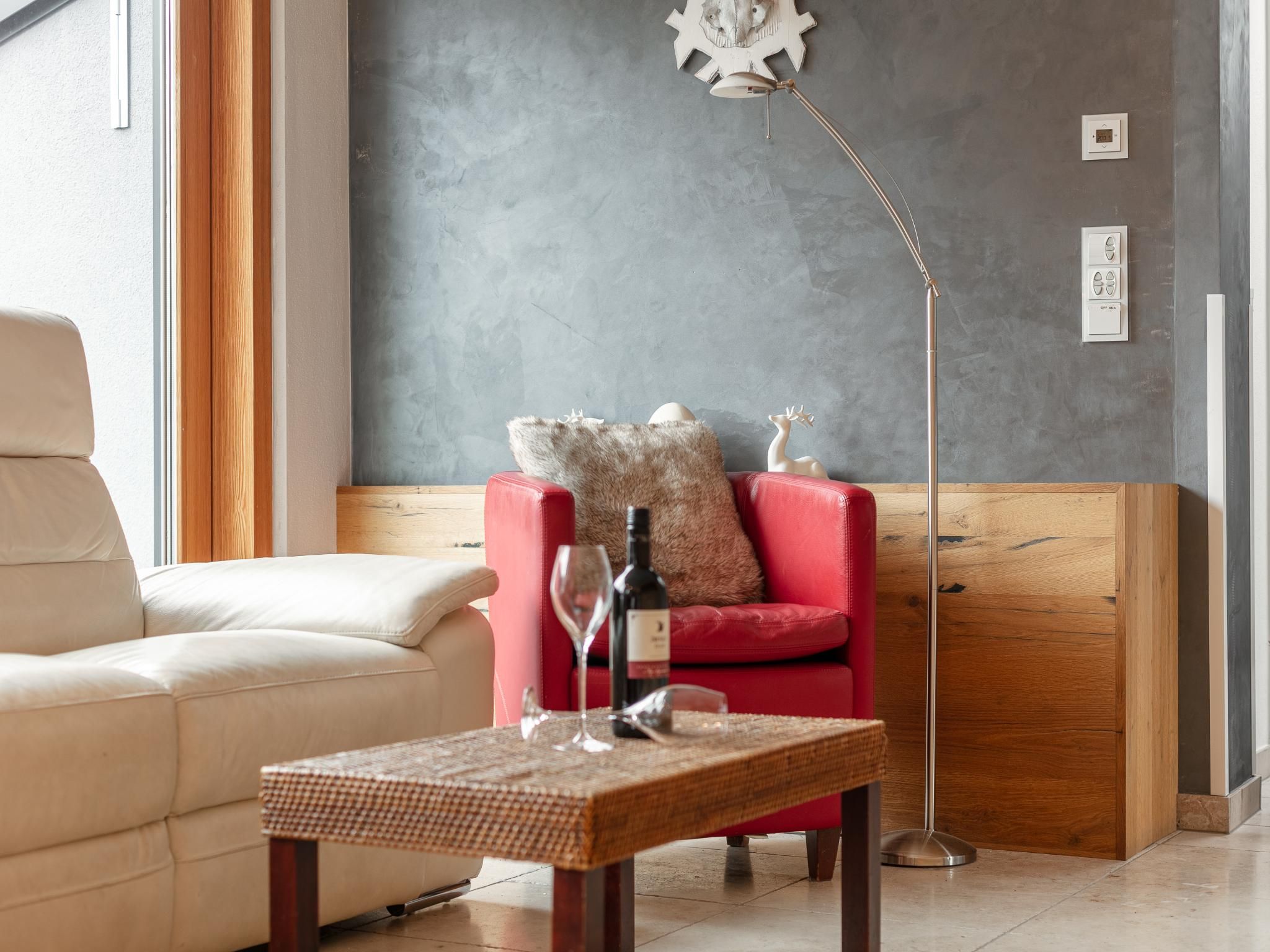 A modern living room with a beige sofa, a red armchair, a wooden coffee table, and a floor lamp.