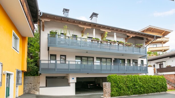 Un edificio de dos pisos con balcón, garaje y un seto bien cuidado.