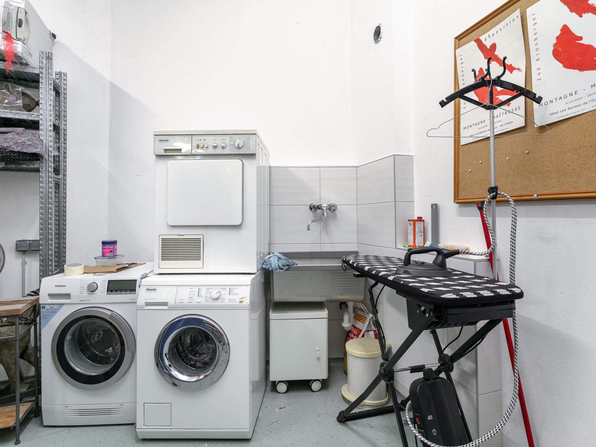 Una sala de lavandería con dos lavadoras, un tendedero y un refrigerador pequeño.