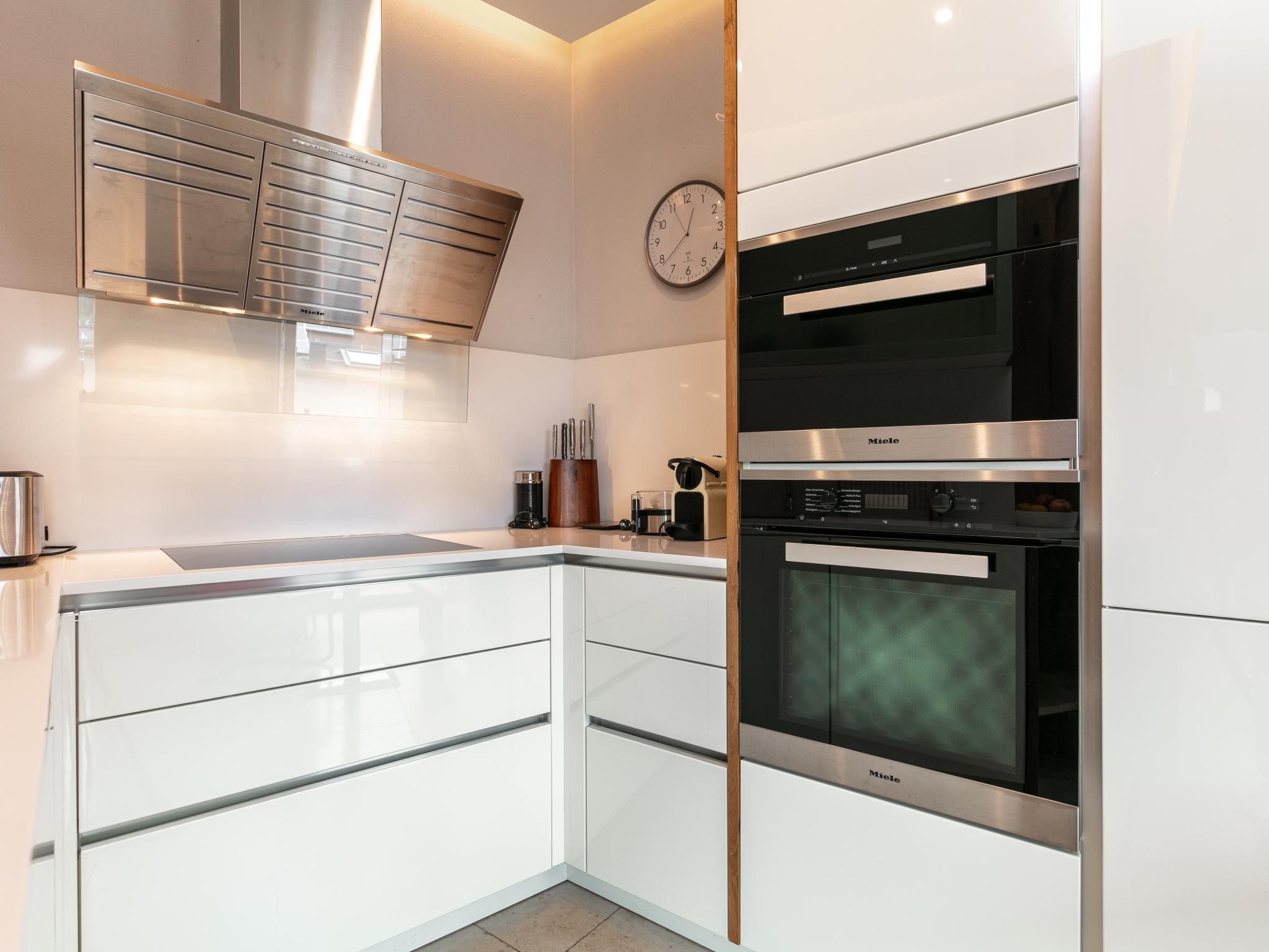 Una cocina moderna con armarios blancos, una campana de acero inoxidable, un reloj y un horno empotrado.