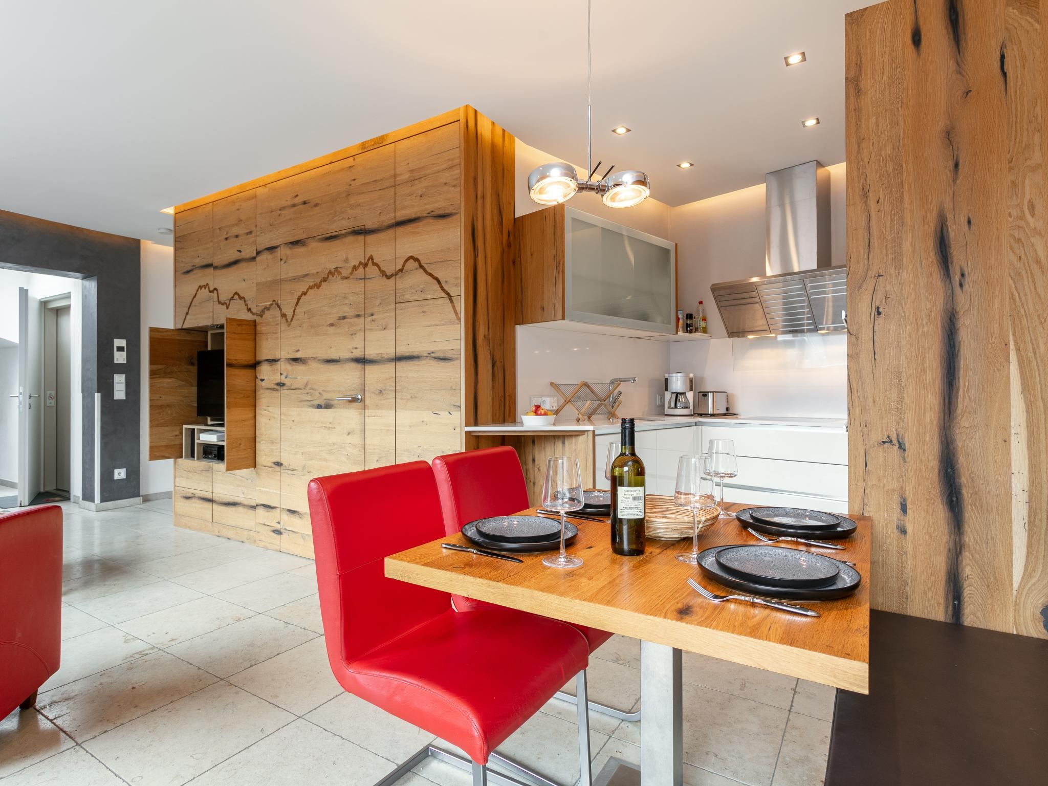 A modern kitchen with wooden accents, a dining table set with plates, glasses, and a bottle of wine.