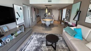 A modern living room with a sofa, a coffee table, a flat-screen TV, and a dining area with a table and chairs. - High Floor 2BR-2BA | Resort & Parking Fee Included (Hollywood)