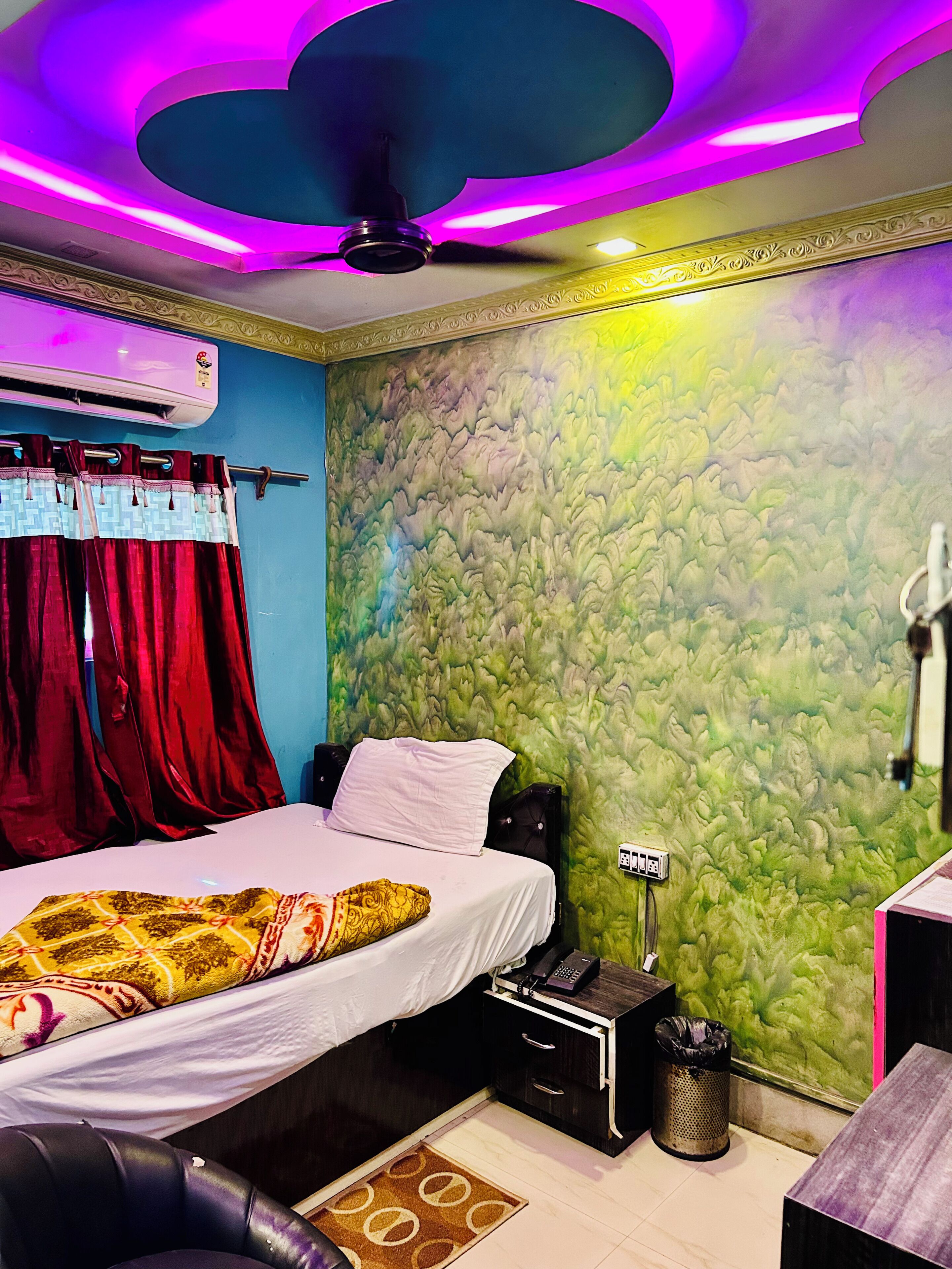 Ein Schlafzimmer mit Bett, Vorhängen, einer Wand mit Strukturmuster, einem Deckenventilator und einem Nachttisch mit Lampe.