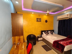 A hotel room with a bed, a desk, a chair, and an air conditioning unit.