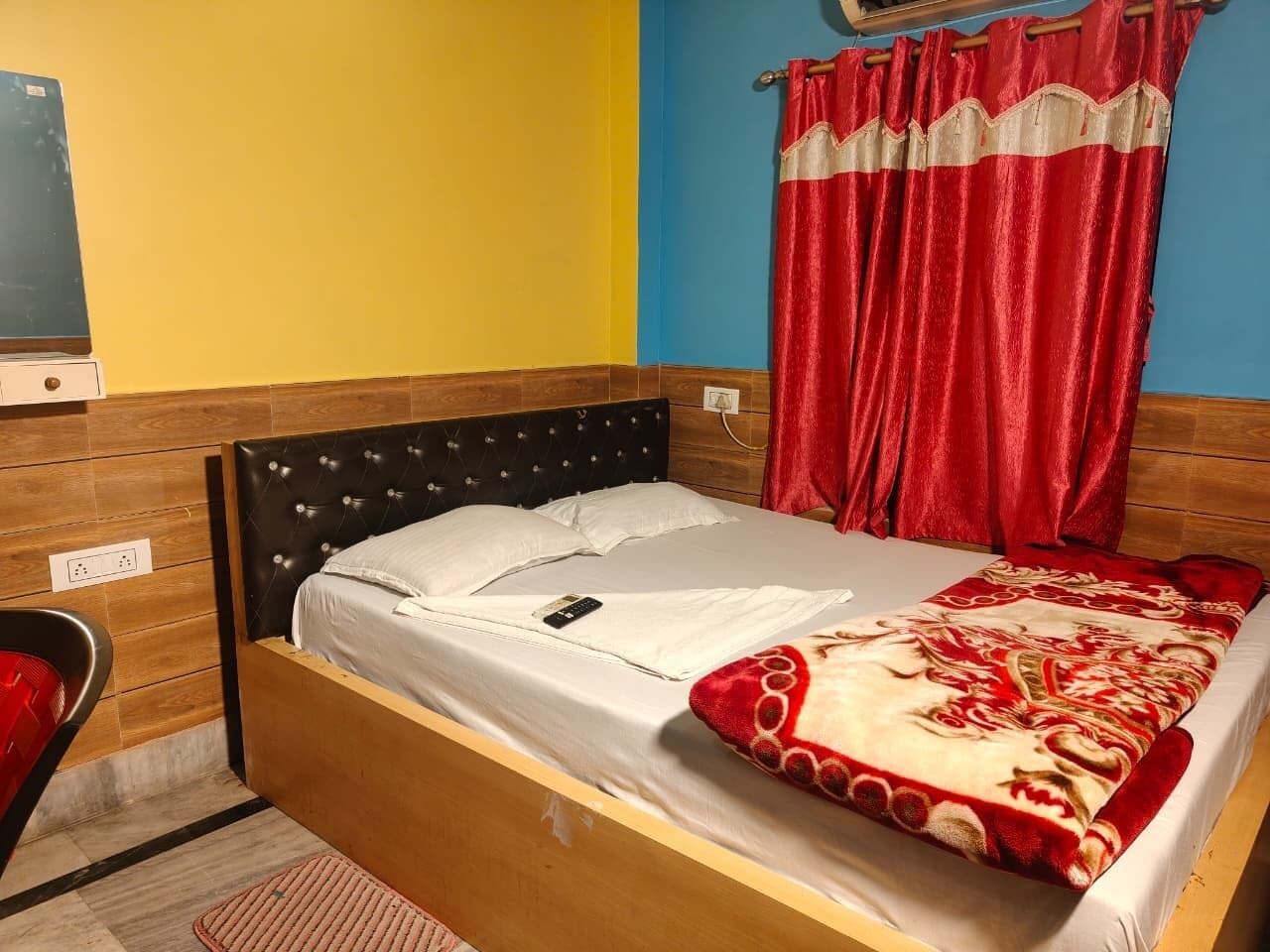 A single bed with a wooden headboard, a white mattress, and a red and beige blanket.