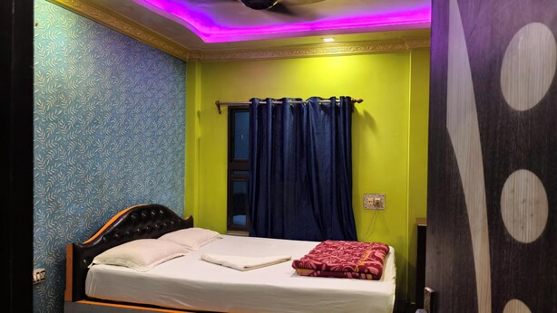 A room with a bed, a window with curtains, a light switch, and a wall with a leaf pattern.