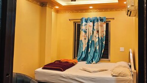 A bedroom with a bed, a ceiling fan, a window with curtains, and a wall-mounted air conditioning unit.