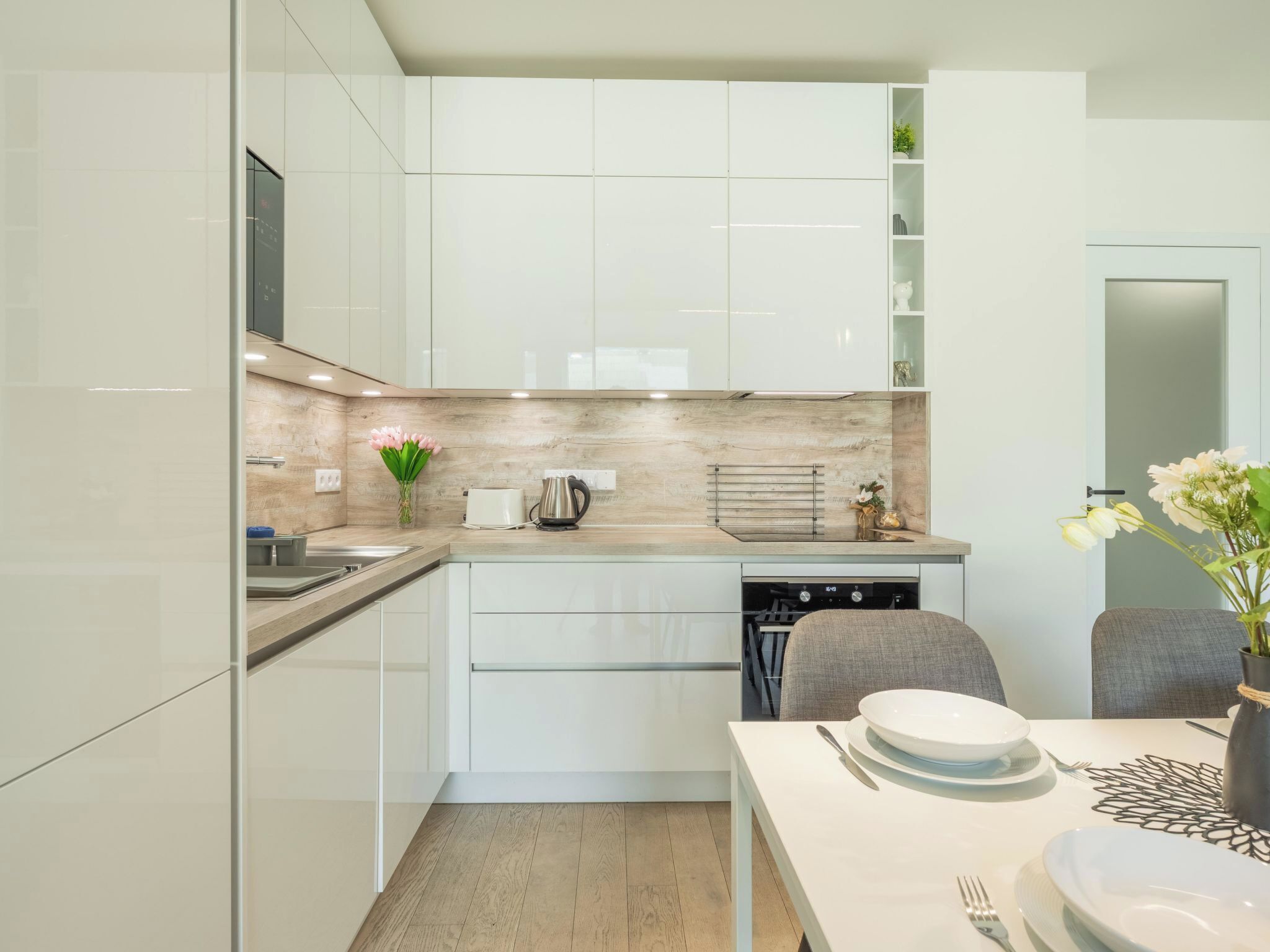 A modern kitchen with white cabinets, a wooden countertop, and a dining area with a table set for two.