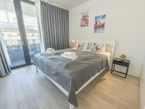 Ein modernes Schlafzimmer mit einem großen Bett, grauen Vorhängen und zwei Bildern an der Wand.