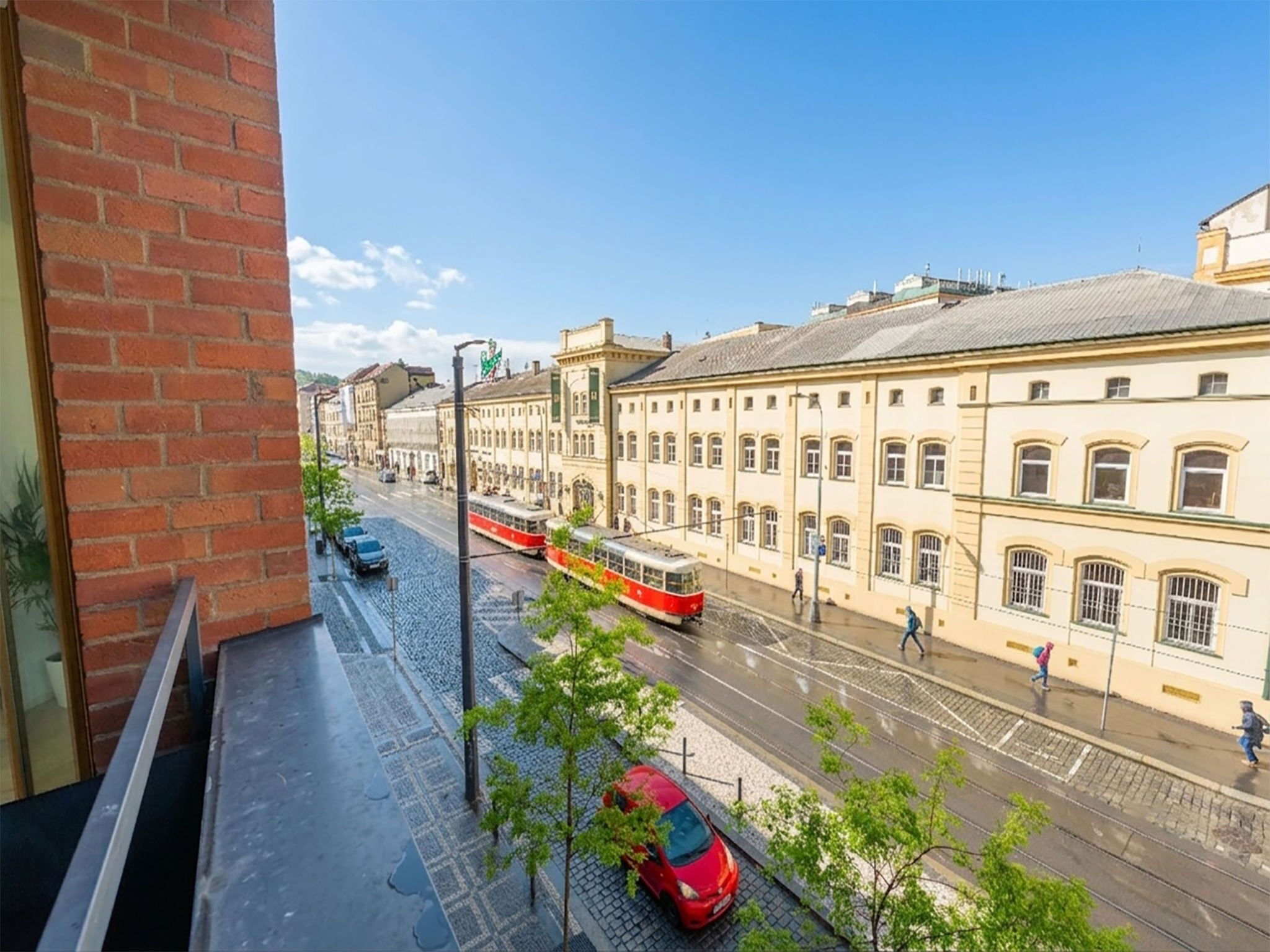 A street view with tram tracks, a red car, and buildings with arched windows.