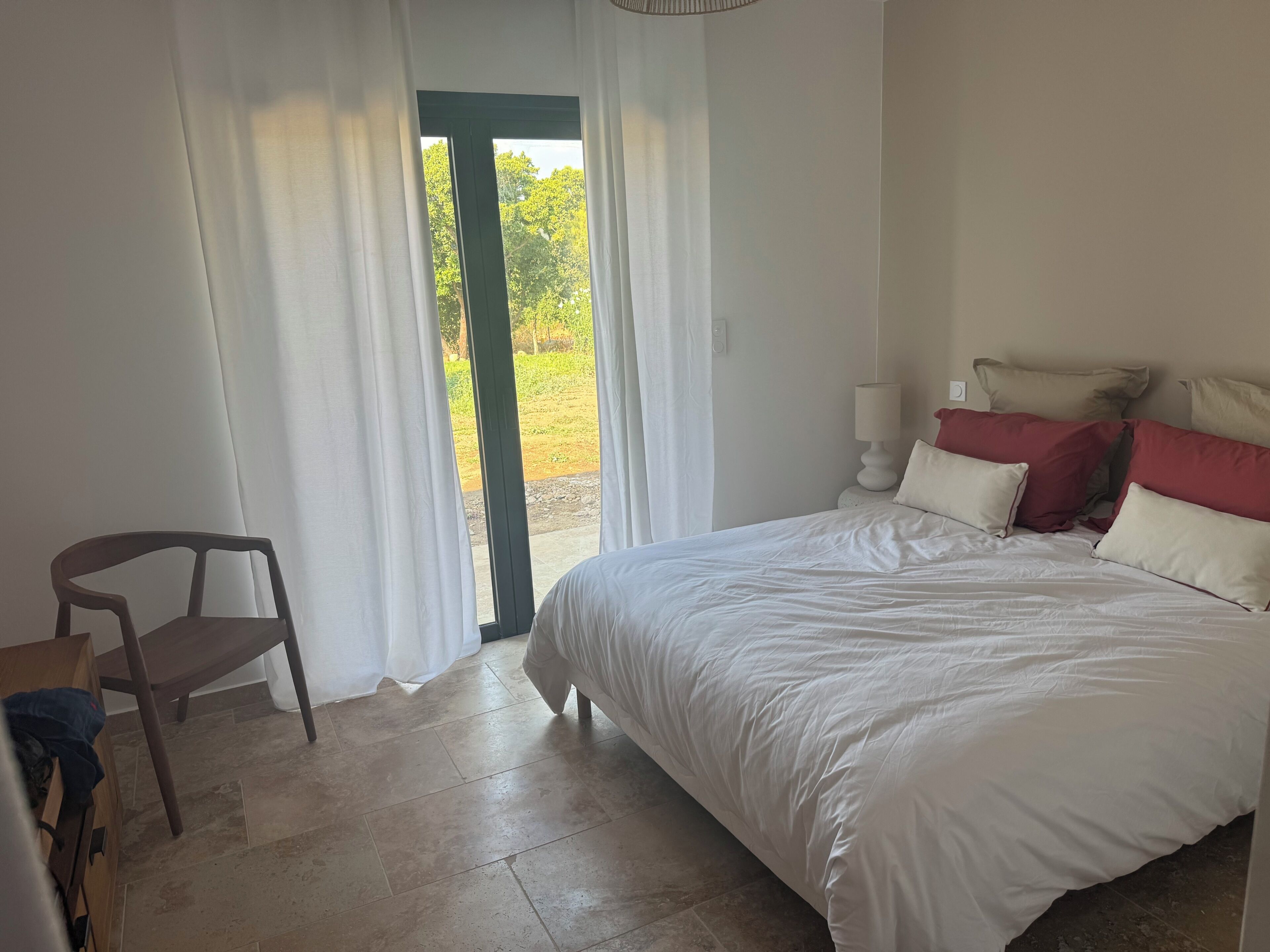 Une chambre à coucher avec un lit, une chaise, une table de chevet et une fenêtre avec des rideaux.