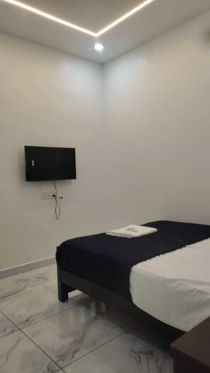 A bedroom with a bed, a flat-screen TV mounted on the wall, and a ceiling light fixture. - TLTA Residency (Aluva)
