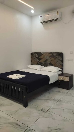 A bedroom with a bed, bedside table, and an air conditioning unit. - TLTA Residency (Aluva)