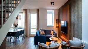 Un salon moderne comprenant un escalier, un ensemble de canapés, un coin repas et un téléviseur fixé à un mur en bois.