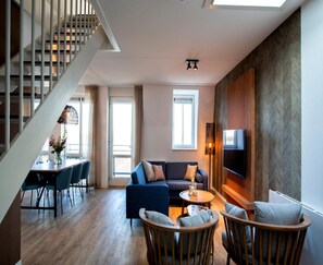 Ein modernes Wohnzimmer mit Treppe, einer Sofagarnitur, einem Essbereich und einem an einer Holzwand befestigten Fernseher.