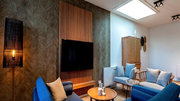 Un salon moderne doté d’un grand téléviseur à écran plat, de canapés bleus, d’un mur d’accent en bois et d’un luminaire au plafond.