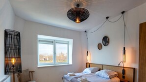 Une chambre à coucher avec un lit, une chaise, une fenêtre et une lampe fixée au mur.
