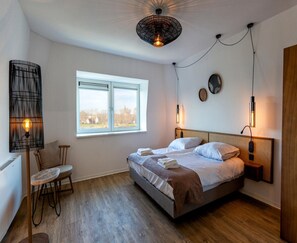 Ein Schlafzimmer mit einem Bett, einem Sessel, einem Fenster und einer Wandlampe.
