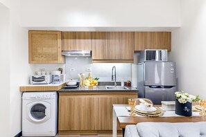 Eine kompakte Küche mit Holzausstattung, einem Edelstahlkühlschrank, einer Mikrowelle, einer Waschmaschine und einem Essbereich mit Tisch für zwei Personen.
