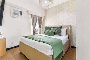 Ein Hotelzimmer mit Bett, einem fensterbelaubten Fenster, einer Wand-Klimaanlage und einem gemusterten Wandteppich.