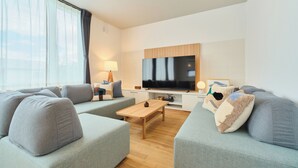 Un salon moderne avec des canapés gris, une table basse en bois, un téléviseur à écran plat et une lampe.