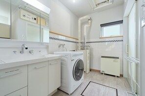 A modern bathroom with a built-in washing machine, a radiator, and a mirror with a control panel. - Suzuran Haus (Higashikawa Kitamachi)
