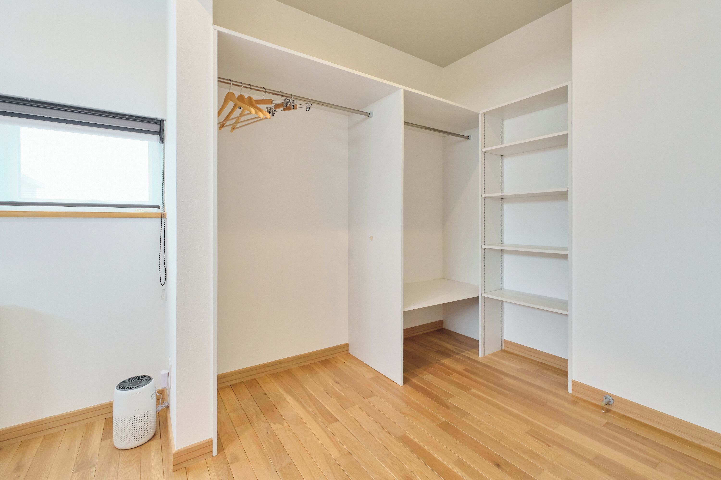 A walk-in closet with wooden flooring, a hanging rod, and built-in shelving.