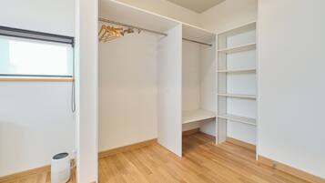 A walk-in closet with wooden flooring, a hanging rod, and built-in shelving.