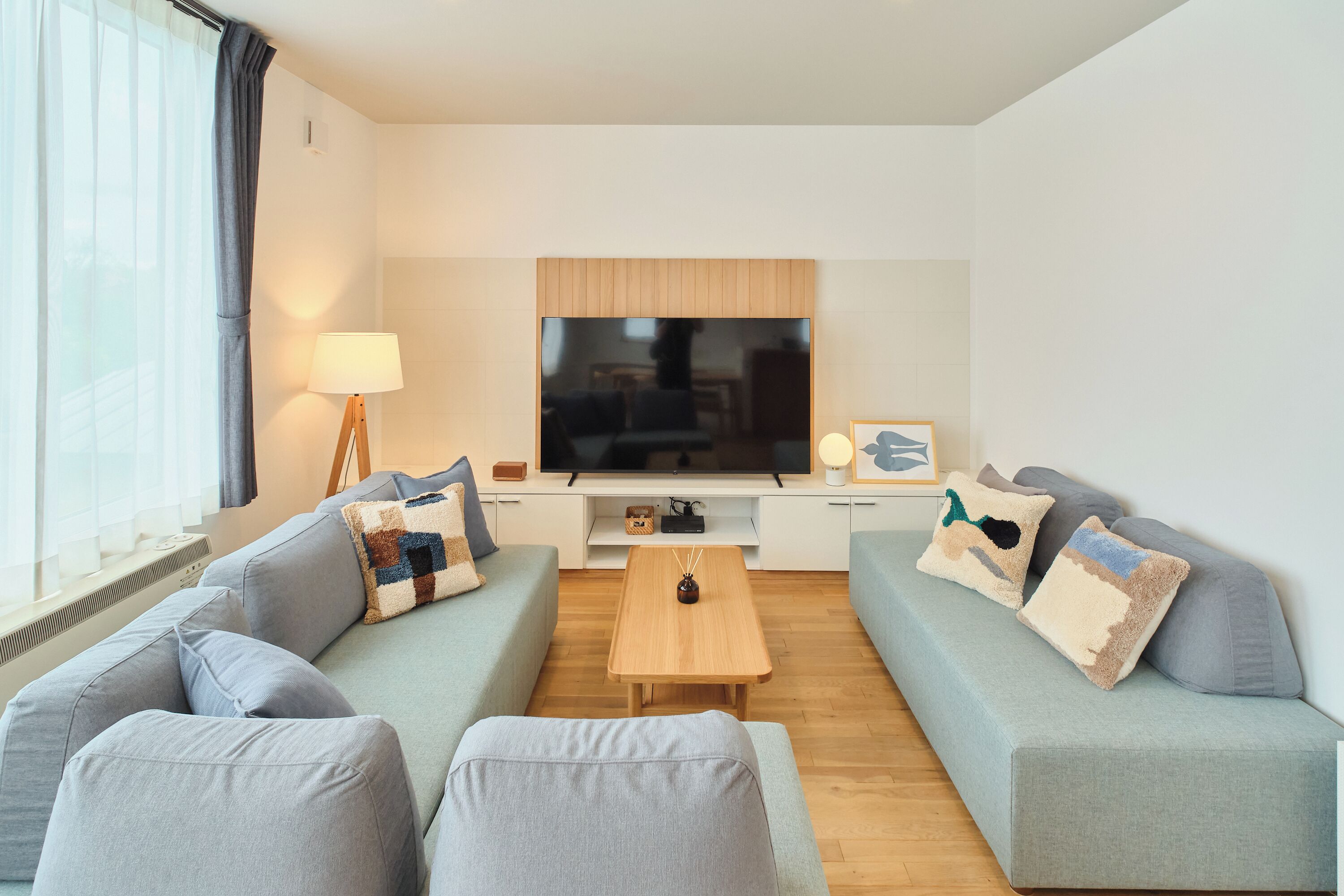 Una sala moderna con un televisor de pantalla plana, dos sofás, una mesa de centro y una lámpara.