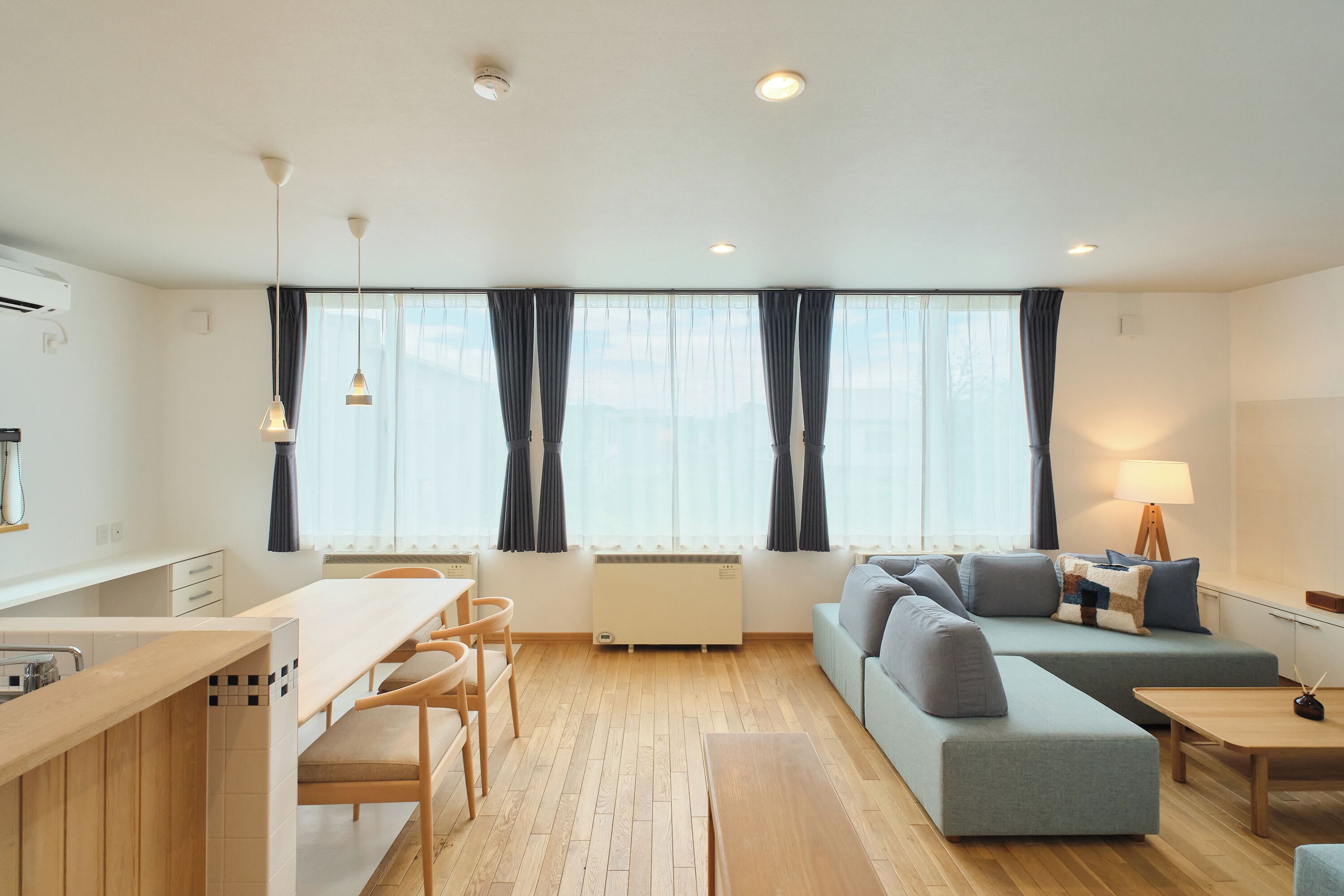 A modern, well-lit living room with a sofa, a dining table, and a kitchen area.