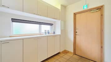 A kitchen with white cabinets, a window with blinds, and a wooden door with an emergency exit sign.
