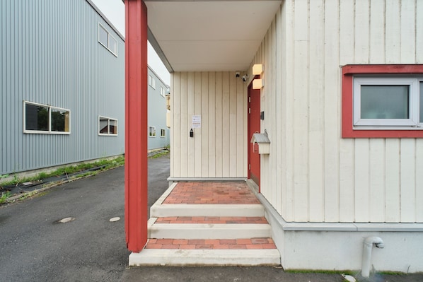 A building with a red and white exterior, a brick-paved entrance, and a narrow pathway leading to a door. - Suzuran Haus (Higashikawa Kitamachi)